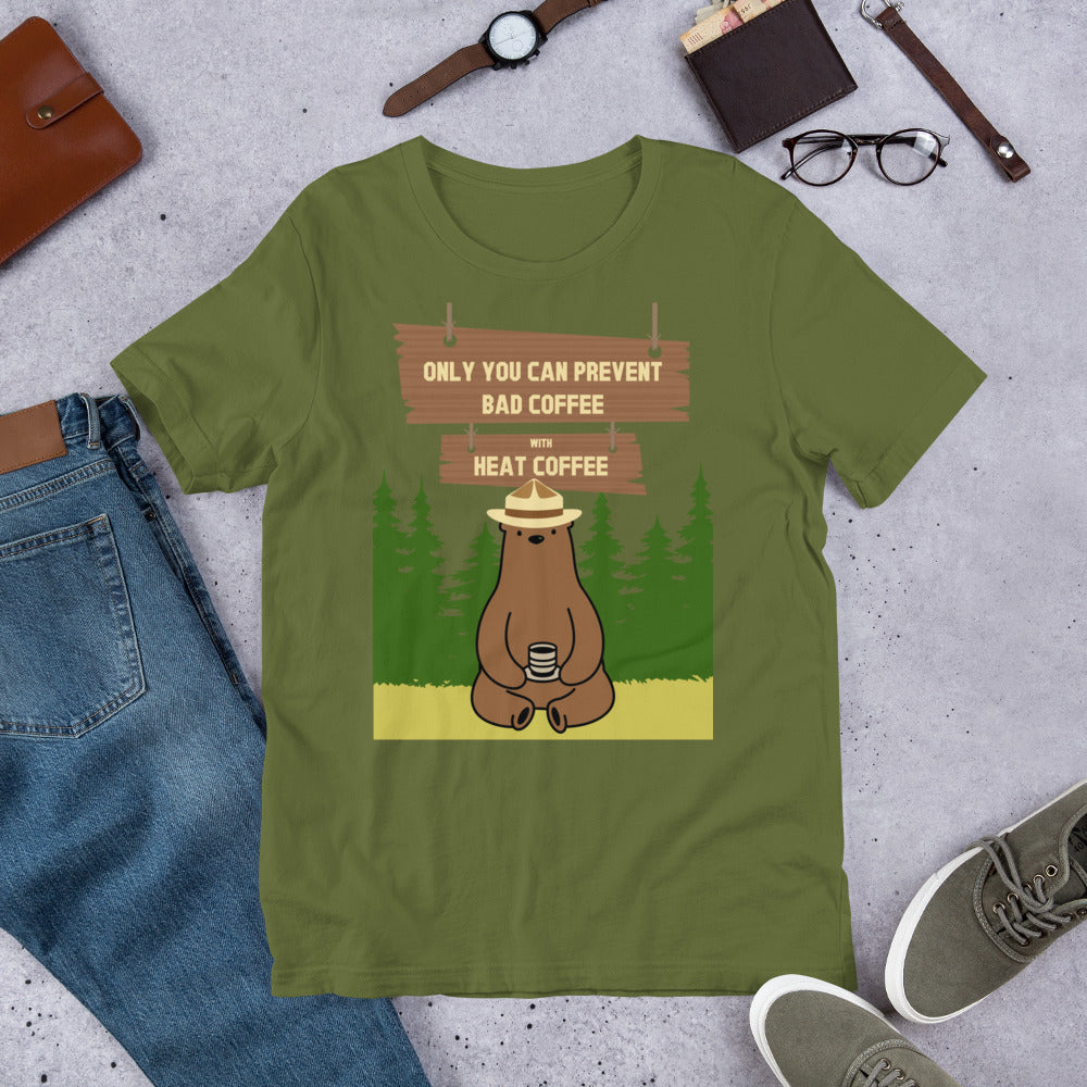A green unisex t-shirt with an illustration of a bear holding a cup of coffee and the text 'Only you can prevent bad coffee' printed on it, displayed flat with a brown hat and glasses on top of the shirt.