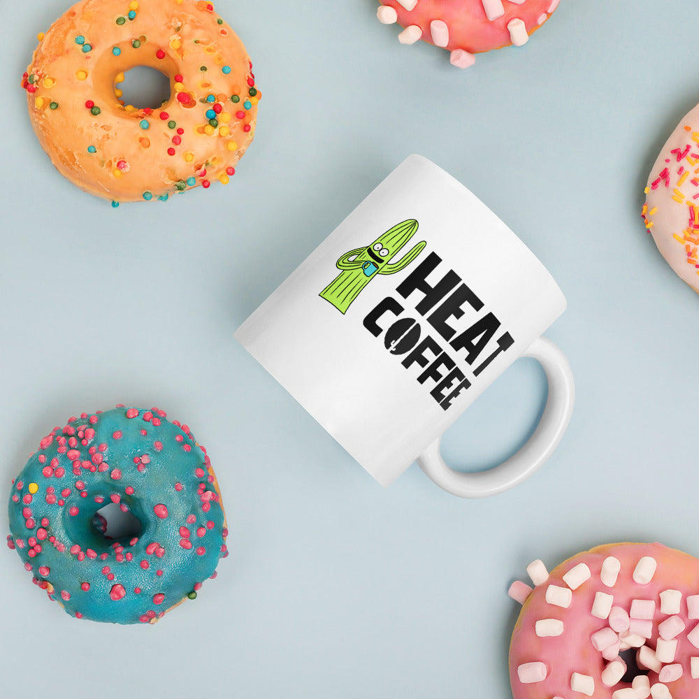 White coffee mug with Heat Coffee logo and cactus character on its side with donuts in the background
